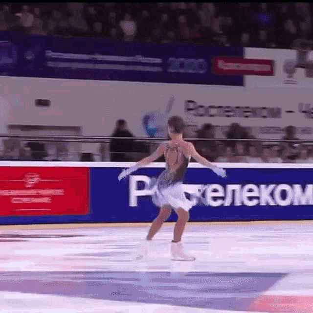 a woman is ice skating in front of a sign that says ' ростелеком '
