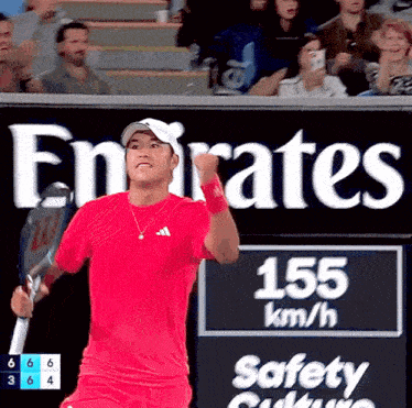 a man in a red shirt is holding a tennis racquet in front of a emirates sign