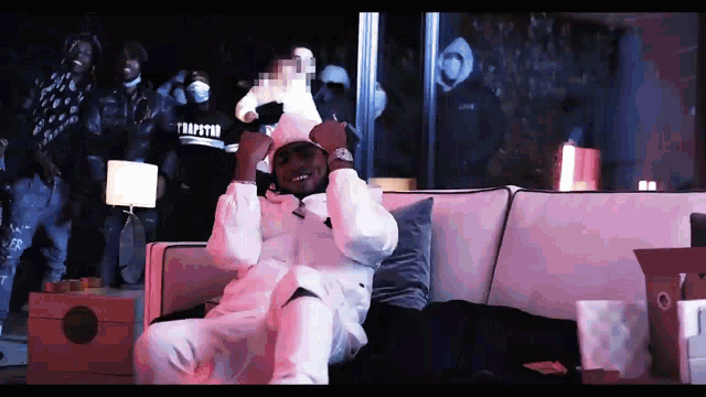 a man sitting on a couch wearing a white jacket that says trapstar on the front
