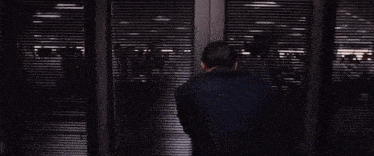a group of people are standing in a hallway behind a row of blinds .