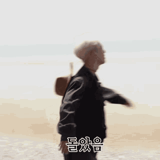 a man in a black jacket is standing on the beach with his arms outstretched .