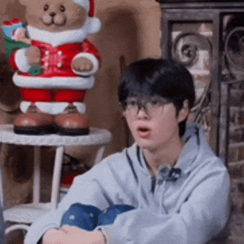 a young man wearing glasses is sitting on the floor in front of a stuffed teddy bear .