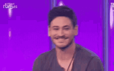a man is clapping his hands on a stage in front of a purple background .