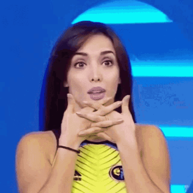a woman in a yellow and black outfit is making a surprised face with her hands on her face .