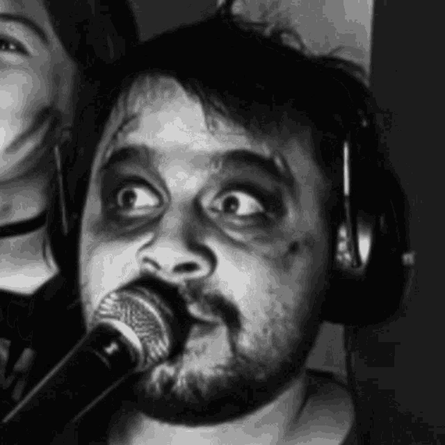 a man with a beard is singing into a microphone with a woman behind him