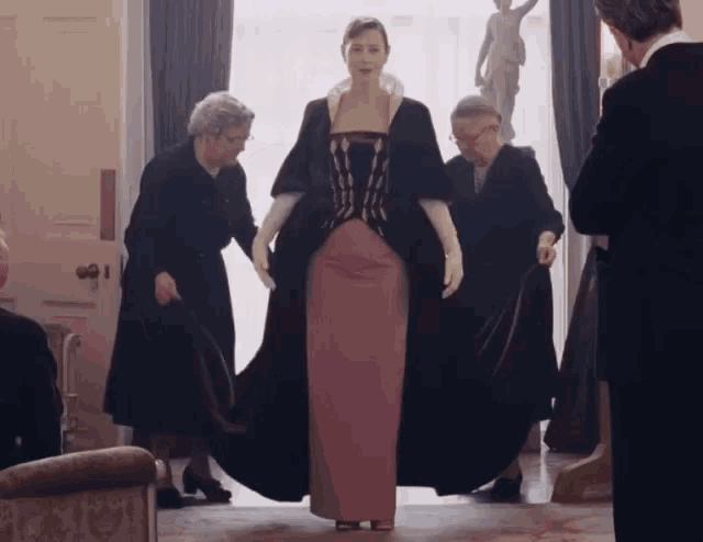 a woman in a pink dress and black coat is being helped by two women
