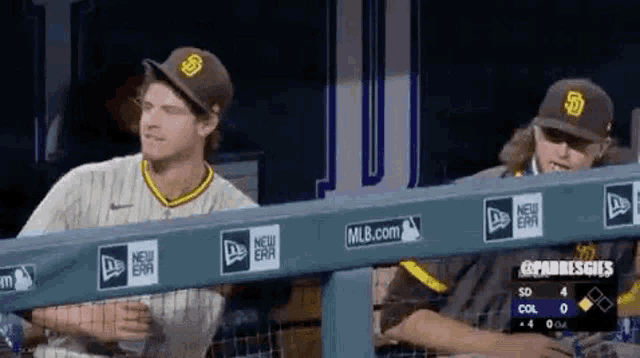 two baseball players are sitting in the dugout during a game .