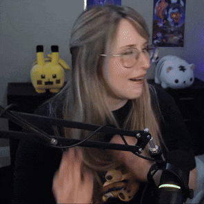 a woman wearing glasses is sitting in front of a microphone with a stuffed pikachu in the background