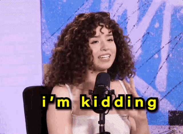 a woman with curly hair is sitting in front of a microphone and says " i 'm kidding "