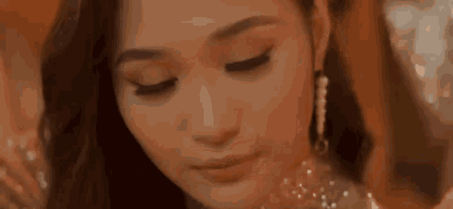 a close up of a woman 's face with her eyes closed . she is wearing earrings and a necklace .