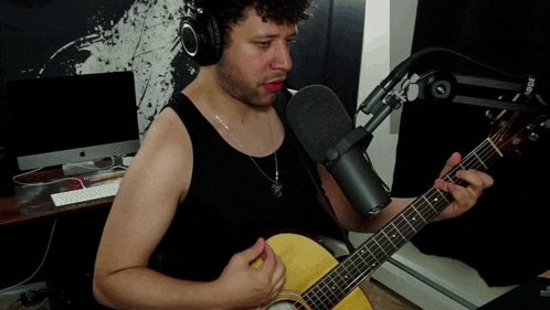 a man wearing headphones is playing a guitar in front of a rode microphone