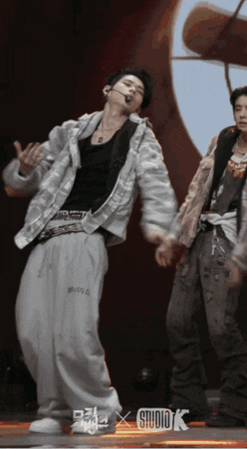a man in a white jacket and grey pants is dancing in front of a sign that says studio k on it