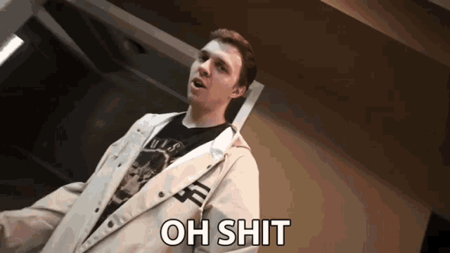a man wearing a white jacket and a black shirt says " oh shit "