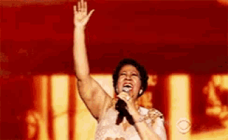 a woman singing into a microphone with her hand up