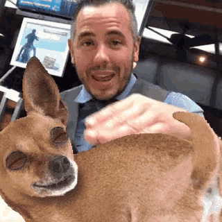 a man is holding a small brown dog and smiling at the camera