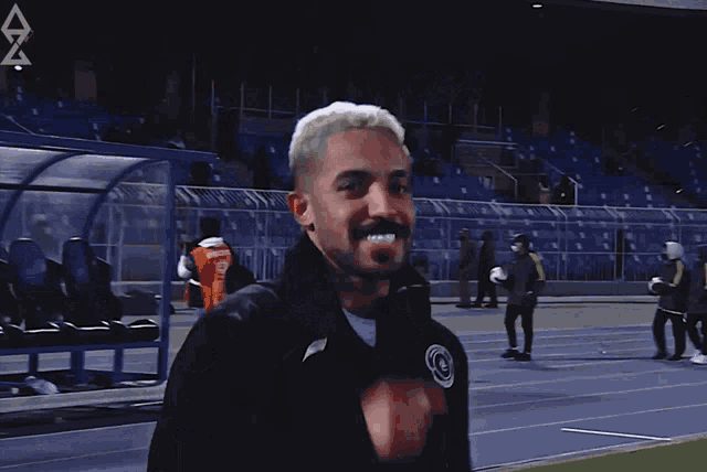 a man wearing a black jacket with a black circle on it stands on a soccer field