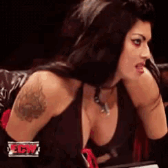 a woman with a tattoo on her shoulder is sitting in front of a sign that says tna