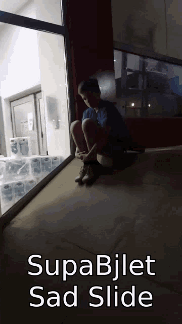 a boy sits on the ground in front of a window with the words supabijlet sad slide on the bottom