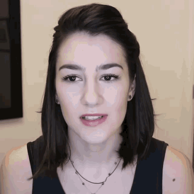 a woman wearing a black tank top and a necklace is looking at the camera