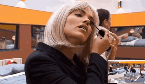 a woman wearing a wig is applying mascara to her eyelashes