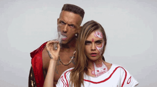 a man smoking a cigarette next to a woman with face paint on her face