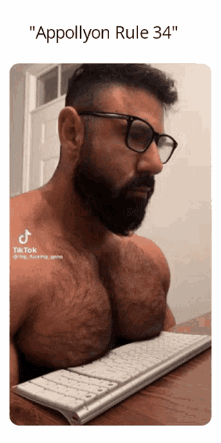 a man with glasses and a beard is sitting at a desk with a keyboard and the caption applillyon rule 34
