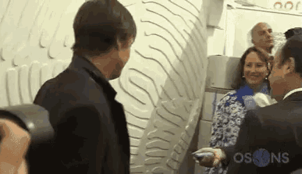 a group of people are standing next to each other in a room with a sign that says os on it .