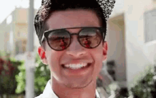 a man wearing sunglasses and a hat is smiling for the camera .