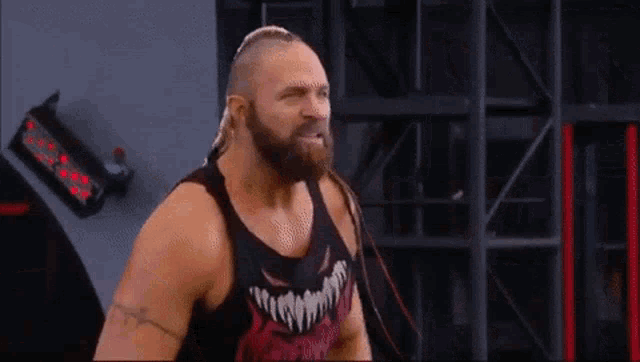 a wrestler with a beard is wearing a tank top with a devil on it .