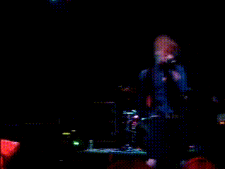 a man singing into a microphone while playing a guitar on stage