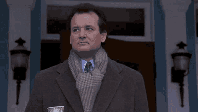 a man in a suit and scarf is standing in front of a door