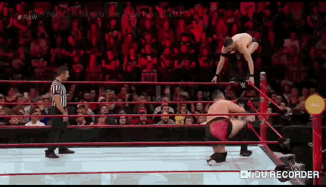 two men are wrestling in a wrestling ring while a referee stands behind them .