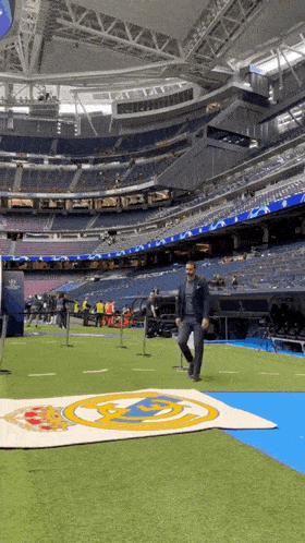 a man in a suit walks on a field in a stadium with empty seats