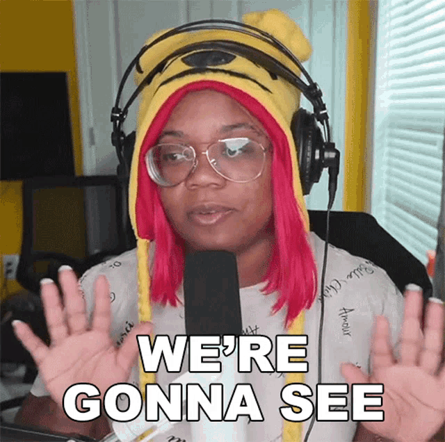 a woman with pink hair wearing headphones and a yellow hat says we 're gonna see