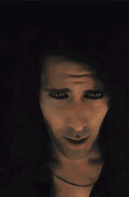 a man with long curly hair has blue eyes and a necklace around his neck