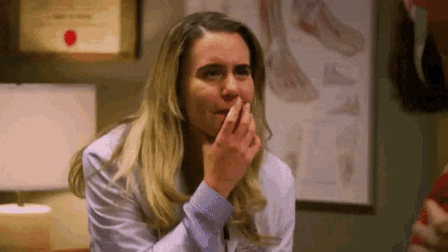 a woman in a white coat is covering her mouth with her hands in a room .