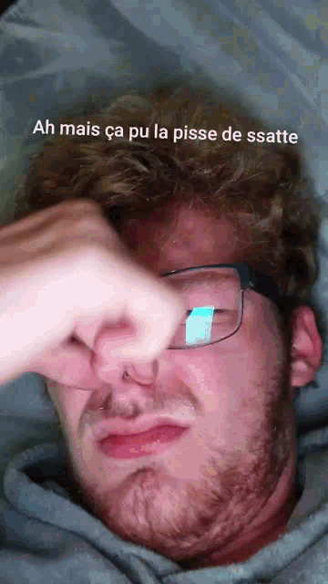 a man with glasses and a beard holds his nose while making a funny face
