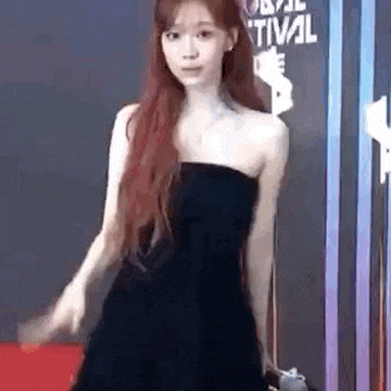 a woman in a strapless black dress is standing on a red carpet .
