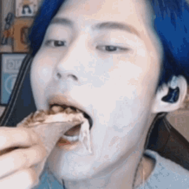a man with blue hair is eating a piece of pizza with his mouth open .