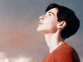 a young man in a red shirt is looking up into the sky