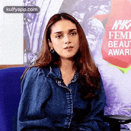 a woman in a denim jacket is sitting in a chair in front of a poster .