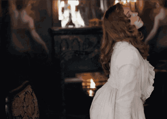 a woman in a white dress stands in a dark room