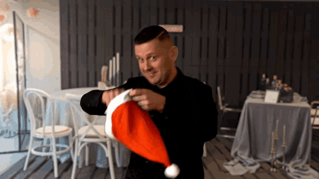 a man in a black suit holds a santa hat