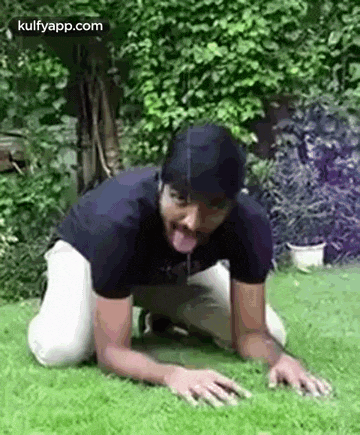 a man is kneeling down on the grass with his tongue out .