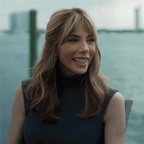 a woman in a black top is smiling in front of a body of water .