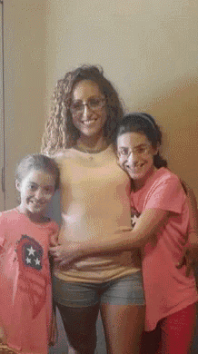 a woman in a pink shirt is hugging two little girls
