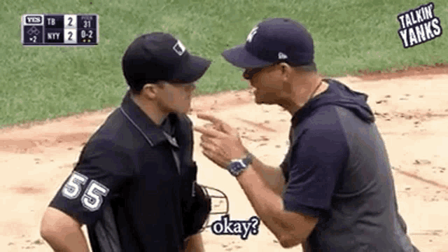 two men are talking to each other on a baseball field and one of them is wearing a shirt with the number 55 on it .