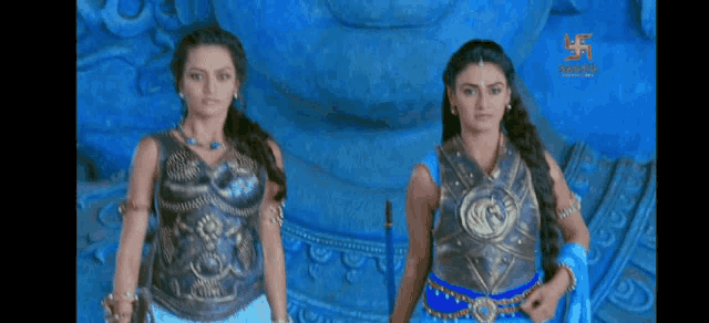 two women in armor are standing next to each other in front of a statue .