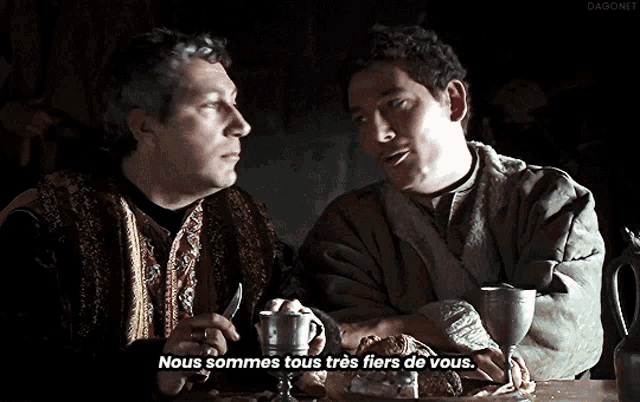 two men are sitting at a table with a caption that says nous sommes tous tres fiers de vous