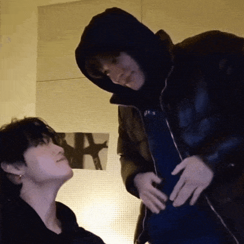 a man in a hooded jacket is touching the belly of another man in a black jacket